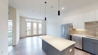 Located at 8680 State Line Rd in Leawood, Kansas, this well-appointed one-bedroom, two-bathroom residence offers a thoughtfully designed open-concept layout with modern finishes throughout. Light-toned hardwood-style flooring runs through the main living areas, creating a bright and cohesive aesthetic.

The kitchen is a standout feature, showcasing a two-tone design with white upper cabinetry and slate-blue lower cabinets, complemented by white quartz countertops, a tile backsplash, and a full suite of stainless steel appliances including a refrigerator, range, microwave, and dishwasher. A central island with pendant lighting provides additional prep space and a natural gathering point that opens into the living room.

The living room is filled with natural light from a set of French doors topped with transom windows that lead to a private balcony with outdoor views. The bedroom features plush carpeting, a ceiling fan, and a wide window that brings in additional natural light. Both bathrooms are finished with gray vanities, white quartz countertops, and clean tile work, with one featuring a full soaking tub and shower combination. A dedicated laundry area with a stacked washer and dryer completes this efficient and modern residence.