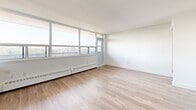 Located on the 8th floor at 3390 Keele St in Toronto's York district, this one-bedroom, one-bathroom unit offers a well-designed layout across a single floor. Light wood laminate flooring runs throughout, complementing the crisp white walls and creating a bright, cohesive aesthetic.

The open-concept kitchen and living area forms the heart of the unit. The kitchen is outfitted with white cabinetry, subway tile backsplash, stainless steel appliances including a full-size refrigerator, and a peninsula island with a dark countertop — ideal for both meal prep and casual dining. The living area benefits from a wall of floor-to-ceiling windows that flood the space with natural light and provide open views of the surrounding Toronto cityscape and treetops.

The bedroom is a well-proportioned private retreat featuring large windows that continue the unit's theme of abundant natural light and outdoor views. A built-in double closet provides ample storage, and the light flooring keeps the room feeling airy and open.

The bathroom is finished with classic white subway tile surrounding a full soaker tub and shower, paired with a stone-topped vanity and tile flooring for a clean, polished look.

The unit also includes a balcony, two hallways for smooth circulation, and baseboard heating throughout. A private outdoor space adds to the overall appeal of this well-appointed Toronto residence.