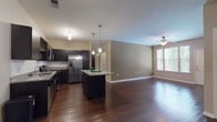 This single-story residence is designed with a contemporary aesthetic, centered around an open-concept kitchen and living area that promotes a seamless flow throughout the main living space. The kitchen is a standout feature, equipped with dark espresso cabinetry, granite countertops, and a full suite of stainless steel appliances, including a French door refrigerator, electric range, microwave, and dishwasher. A central island with a matching granite surface provides additional workspace and casual seating, while pendant lighting above adds a polished finishing touch. Rich, dark hardwood-style flooring extends throughout the kitchen and living areas, creating a warm and cohesive look.

The bedrooms are carpeted for comfort and each include ceiling fans. One bedroom benefits from a large window that brings in natural light and outdoor views, while the other features a generous walk-in closet outfitted with wire shelving for practical storage. Both bathrooms are consistently finished with dark vanity cabinetry, granite countertops, and tub-shower combinations with tile surrounds. Hardwood-style flooring continues into the bathrooms, maintaining a unified design. A dedicated laundry closet houses a full-size top-load washer and dryer, adding everyday convenience to this well-appointed space.