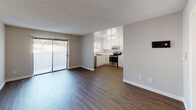 Unit #102 at 2925 Broadway in San Diego is a single-story residence featuring a practical, well-organized layout. The open-concept living area is a central highlight, finished with durable wood-style plank flooring and neutral gray walls that create a clean, versatile backdrop. A textured ceiling runs throughout the main living space, adding subtle visual interest. Large sliding glass doors along one wall of the living area allow natural light to filter in and provide a view of the surrounding outdoor landscape, enhancing the sense of openness.

The kitchen is positioned adjacent to the living area in an open pass-through configuration, making the space feel connected and functional. It features white cabinetry extending to the ceiling for ample storage, light countertops, a stainless steel range, dishwasher, refrigerator, and an under-cabinet range hood. A window above the sink brings in additional natural light.

The bedroom is a well-proportioned, quiet space with plush carpeting, neutral walls, and a window fitted with horizontal blinds that allow controlled natural light. The bathroom includes a full tub-shower combination with clean white fixtures, maintaining a simple and functional design throughout.
