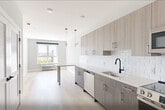 Unit 503 at 1213–1221 Broad St is a thoughtfully designed one-bedroom, one-bathroom residence that blends modern aesthetics with functional living. Light ash hardwood flooring flows throughout the open living areas and bedroom, creating a warm and cohesive feel across the space.

The kitchen is a standout feature, outfitted with contemporary flat-panel cabinetry in a warm gray wood-grain finish, complemented by light quartz countertops and a classic white subway tile backsplash. Stainless steel appliances — including a range, microwave, dishwasher, and refrigerator — are paired with a matte black faucet and hardware, adding a sharp, modern contrast.

The bedroom offers a comfortable and private retreat, featuring a large window that invites natural light and provides views of the surrounding neighborhood. A set of double doors leads to a spacious closet, while a single door provides access to the rest of the unit.

The bathroom features large-format tile flooring in a soft neutral tone, matte black fixtures and grab bars, and a clean, minimalist design that prioritizes both style and accessibility.

Throughout the unit, crisp white walls, white panel doors with matte black hardware, and consistent finishes create a polished, contemporary atmosphere ideal for modern urban living.