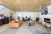 This well-appointed single-floor commercial space combines professional functionality with thoughtful interior design. The standout architectural feature throughout is the striking coffered wood ceiling with recessed lighting, which adds warmth and a refined character to every area of the space.

The main lounge and reception area centers around a richly toned leather sofa, a circular glass-top coffee table, and a vibrant multi-colored area rug that anchors the room. A beverage station with a coffee maker and sideboard provides a welcoming amenity for guests and staff alike. Bold abstract wall art and decorative greenery add personality to the soft blue-gray walls.

Adjacent to the lounge, a dedicated workspace features dual desks, ergonomic seating, and workstations — ideal for day-to-day office operations. This area also includes a wall-mounted flat-screen television above a sleek, white-tiled linear fireplace flanked by two patterned accent chairs, creating a sophisticated focal point.

A separate dining or conference nook offers a small table with upholstered chairs, bathed in natural light from large sliding glass doors and windows fitted with blinds. The combination of tile and carpet flooring defines each functional zone, while the consistent wood coffered ceiling ties the entire space together into a cohesive, professional environment.