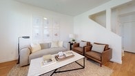 This two-story home offers a clean, modern aesthetic throughout, characterized by crisp white walls, hardwood-style flooring on the main level, and an abundance of natural light streaming through slatted window blinds. The kitchen is a functional centerpiece, outfitted with white shaker cabinetry, granite countertops, black appliances including a gas range, built-in microwave, and refrigerator, and a peninsula with seating that connects seamlessly to the dining area. The dining space comfortably accommodates a round table and chairs, bathed in natural light from dual windows. The living room is bright and welcoming, featuring a large window with views of the surrounding greenery. The primary bedroom is generously sized, with soft carpeting, ample room for a king-sized bed, and access to a spacious walk-in closet equipped with wire shelving systems. A secondary bedroom offers similar comfort with carpeted floors and natural light. The shared bathroom is well-finished, featuring granite countertops, white cabinetry, a combined shower and soaking tub, and warm hardwood-style flooring. A dedicated laundry room with side-by-side washer and dryer units and built-in shelving adds everyday convenience to this thoughtfully designed home.