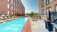 Located at 1531 S Eighth St in the Soulard neighborhood of St. Louis, Missouri, this outdoor amenity space is a standout feature set against the backdrop of a striking, multi-story historic brick building. The architecture showcases classic industrial-era design, with rows of large, arched and rectangular windows lining the facade — a hallmark of St. Louis's adaptive reuse developments.

The centerpiece of this outdoor space is a generously sized swimming pool with crystal-clear blue water, framed by a broad brick-tiled pool deck. The deck is well-appointed with multiple lounge chairs and chaise lounges, providing ample space for relaxation and sunbathing. Potted plants and greenery are thoughtfully placed throughout, adding natural color and softening the hardscape surroundings.

A dedicated grilling and outdoor dining area is positioned along one side of the pool, complete with gas grills and seating — ideal for outdoor gatherings and social events. The space is enclosed by a wrought iron fence, offering both security and an open, airy feel that allows views of the surrounding mature trees and neighborhood beyond.

The combination of the warm brick building facade, vibrant landscaping, and well-maintained pool facilities creates a welcoming and functional outdoor retreat, blending the character of historic St. Louis architecture with modern residential amenities.