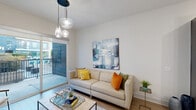 Located in the vibrant McKinney Avenue corridor of Dallas, this well-appointed one-bedroom, one-bathroom residence offers a thoughtfully designed open-concept layout across a single floor. The combined kitchen and living area serves as the heart of the home, featuring wood-look flooring, soaring ceilings, and a wall of sliding glass doors that flood the space with natural light and open onto a private balcony with outdoor views. The kitchen is outfitted with dark espresso cabinetry, quartz countertops, a marble-style tile backsplash, stainless steel appliances including a full-size refrigerator and range, and a peninsula island with built-in shelving and bar seating. Pendant lighting and a track lighting system complete the contemporary aesthetic. The living area is anchored by a stylish chandelier and provides direct balcony access. The spacious bedroom features plush carpeting, a large window admitting ample natural light, and a dedicated closet. The full bathroom offers a wide vanity with quartz countertops, dark wood cabinetry, tile flooring, and a soaking tub with shower combination. Clean white walls and modern finishes throughout contribute to a bright, cohesive, and move-in-ready ambiance.