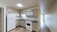 This studio offers a thoughtfully designed single-level layout that maximizes functionality and comfort. The kitchen is a standout feature, showcasing gray cabinetry with brushed metal hardware, dark countertops, and a classic white subway tile backsplash that adds a timeless, clean aesthetic. White appliances — including a gas range, over-the-range microwave, refrigerator, and sink — are seamlessly integrated into the cabinetry, providing all the essentials for everyday living. Ample upper and lower cabinet storage ensures plenty of space for organization. The kitchen flows naturally into the open living area, which is bathed in natural light streaming through a large window. Hardwood-style flooring runs throughout the space, lending a warm and cohesive feel to the entire unit. The open-concept design creates a sense of spaciousness, making the studio feel inviting and versatile. Neutral wall tones and quality finishes throughout contribute to a bright, move-in-ready environment that is both practical and comfortable for everyday living.