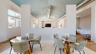 This single-floor community clubhouse is thoughtfully designed with a contemporary aesthetic, blending open, airy spaces with stylish, functional areas throughout. The welcoming entrance features soaring ceilings, wood-look tile flooring, and expansive glass doors that flood the space with natural light and provide views of the surrounding community and pool area.

The main lounge area is appointed with warm hardwood-style flooring, floor-to-ceiling windows, and direct outdoor access, offering bright, open seating with a relaxed yet refined atmosphere. A bold pendant light anchors the space, complementing the neutral palette and modern furnishings.

The game room is a standout feature, boasting dramatic vaulted ceilings painted in a soft teal, exposed ductwork as an industrial design element, and a vibrant bold-patterned accent wall in orange and white. A full-size pool table and shuffleboard table make it an ideal social hub. Built-in open shelving, a wood-paneled feature wall, and a mounted flat-screen TV add warmth and function.

The dining area transitions between tile and wood-look flooring, featuring glass-top tables with gold pedestal bases and woven accent chairs beneath elegant chandelier lighting and a teal vaulted ceiling.

A sleek kitchenette rounds out the space with white shaker cabinetry, gold hardware, stone-look countertops, a textured tile backsplash, and a mounted television — ideal for community gatherings and events.