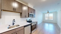 Located at 103 East 2nd Street in Richmond, VA, this modern one-bedroom, one-bathroom unit offers a thoughtfully designed open-concept layout across a single floor. The kitchen is a standout feature, equipped with stainless steel appliances including an electric range, built-in microwave, and dishwasher. Rich dark-toned cabinetry with matte black hardware contrasts elegantly with the white quartz countertops and classic subway tile backsplash. A deep stainless steel sink with a matte black faucet completes the functional and stylish cooking space. The kitchen flows seamlessly into the living area, which features light wood-style flooring, a ceiling fan, and a glass door that opens to a balcony, inviting in generous natural light and outdoor views of the surrounding Richmond cityscape. The bedroom is carpeted for comfort and includes a ceiling fan, bright windows with views, and access to a dedicated closet. The bathroom is well-appointed with a wide dark-wood vanity, white countertop, large mirror with overhead lighting, wood-style tile flooring, and matte black fixtures throughout. Clean white walls and modern finishes lend a cohesive, contemporary ambiance to the entire unit.
