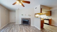 This single-floor residence offers a practical and comfortable layout with a warm, neutral aesthetic carried throughout. The living area serves as the heart of the home, highlighted by a striking corner fireplace clad in natural stone with a clean white mantel above — a standout architectural feature that adds character and coziness to the space. A ceiling fan overhead and wood-look laminate flooring underfoot complete the inviting atmosphere.

The kitchen is positioned adjacent to the living area, separated by a half-wall breakfast bar that maintains an open, connected feel. The galley-style kitchen is well-equipped with warm-toned wood cabinetry, ample upper and lower storage, a double-basin sink, electric range, dishwasher, and a full-size refrigerator. A textured ceiling and under-cabinet ventilation add functional detail.

Two bedrooms each feature the same wood-look flooring, ceiling fans with lighting, neutral wall tones, and windows fitted with blinds that allow for natural light and privacy. The rooms are well-proportioned and versatile in use.

The bathrooms are clean and functional, each featuring a full tub-shower combination with tiled surrounds and chrome fixtures. The overall design of the space prioritizes functionality, with a consistent and cohesive neutral palette throughout.