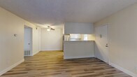 Located at 2930 Linden Ln in Carmichael, CA, this one-bedroom, one-bathroom residence offers a well-designed single-floor layout with light-toned laminate wood flooring throughout. The open-concept living, dining, and kitchen area forms the heart of the home, anchored by a classic fireplace with a tiled hearth and sliding glass doors leading to a private balcony with views of mature surrounding trees. Ceiling fans provide additional comfort in the main living area. The kitchen features a peninsula counter with upper and lower white cabinetry, stainless steel refrigerator, electric range, dishwasher, and a window above the sink that brings in natural light. The spacious bedroom offers ample room for furnishings, a mirrored sliding-door closet, and a large window with pleasant green views. The bathroom includes a full-size soaking tub and shower combo with a grab bar and clean white tile surround. Additional spaces include a utility room, hallway, and dedicated closet storage. Textured ceilings are present throughout, and the neutral color palette gives the space a bright, clean, and move-in ready feel.
