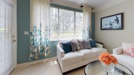 This single-story residence offers a thoughtfully designed layout with a cohesive coastal-inspired color palette throughout. The living room serves as a central gathering space, featuring a large window with sheer floral drapes that frame outdoor greenery views, tiled flooring, and a teal accent wall that lends warmth and character to the room.

The dining area adjoins the living space and is bathed in natural light from a window dressed with a decorative valance. Light tile flooring continues through this space, complementing the warm yellow walls. The galley-style kitchen features light wood cabinetry, a double sink, full suite of white appliances including a dishwasher, electric range, and microwave, along with rich hardwood flooring.

The bedroom offers plush carpeting, a teal accent wall, natural light from a window with sheer curtains, and an open closet with shelving. A dedicated in-unit laundry room houses a full-size washer and dryer alongside wire shelving and a water heater.

The full bathroom includes hardwood flooring, a single vanity with a framed mirror, and a tub-shower combination with a curtain enclosure. Throughout the residence, white panel doors with brass hardware provide classic finishing details.