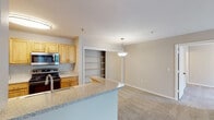 This single-floor residence offers a practical and comfortable layout designed for everyday living. The open-concept kitchen and living area form the heart of the home, where light wood-toned cabinetry, granite-style countertops, and a full suite of stainless steel appliances — including a refrigerator, electric range, built-in microwave, and dishwasher — are complemented by easy-care hardwood-style flooring. A curved breakfast bar peninsula provides additional prep space and casual seating, while a pendant light above adds a decorative touch. The adjacent living area is finished with plush neutral carpet and flows seamlessly through the space, with a tiled entry foyer visible from the main corridor. Two bedrooms feature ceiling fans with light fixtures, large windows with vertical blinds for natural light and privacy, and generous walk-in closets with built-in shelving. Both bathrooms are similarly appointed, each offering a full tub-shower combination with white tile surround, a wood-toned vanity with an integrated sink, and rich dark slate-style tile flooring. Additional storage is provided by open shelving visible in the living area. The neutral color palette throughout creates a calm, cohesive ambiance well-suited to a variety of furnishing styles.