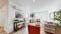 This single-story, two-bedroom, two-bathroom residence in Brentwood, California, offers a thoughtfully designed layout with a clean, contemporary aesthetic throughout. Light wood-tone flooring runs continuously across all rooms, lending a cohesive and airy feel to the entire space.

The living room serves as the heart of the home, featuring crisp white walls, recessed lighting, a wall-mounted mini-split climate control unit, and large windows fitted with horizontal blinds that allow abundant natural light to fill the room. A door provides direct access to an outdoor area. The open arrangement accommodates generous seating and decorative elements comfortably.

The kitchen is well-appointed with rich, dark wood cabinetry, granite-style countertops, and stainless steel appliances including a range, microwave, and dishwasher, along with a deep undermount sink.

Both bedrooms are generously proportioned, bright spaces with large windows offering outdoor views of the surrounding Brentwood neighborhood, including glimpses of palm trees. The primary bedroom benefits from a spacious walk-in closet with full-length hanging rods. The bathrooms maintain the home's clean aesthetic with wood-toned vanities and light, neutral finishes throughout.