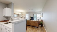 This well-appointed one-bedroom, one-bathroom apartment in Langhorne, PA offers a thoughtfully designed single-floor layout that maximizes every square foot. Light hardwood-style flooring flows throughout, tying together the open-concept living, dining, and kitchen areas. The living room is bright and airy, with sliding glass doors leading to a private balcony and views of the surrounding community. The kitchen features white cabinetry, white quartz countertops, stainless steel appliances, and a peninsula with bar seating — ideal for casual dining. Adjacent to the kitchen, the dining area is anchored by a chandelier and offers a cozy, defined space for meals. A dedicated office provides a quiet retreat with a large window that draws in natural light. The bedroom is a serene space with dual windows, soft neutral tones, and comfortable proportions. The bathroom includes a white vanity with ample counter space, clean finishes, and a tub-shower combination. Neutral gray walls throughout the unit lend a cohesive, modern feel, while the entrance provides a welcoming transition into the home. This apartment balances functional living with a comfortable, inviting ambiance.