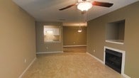 This single-story space presents an open-concept layout that seamlessly connects the living, dining, and kitchen areas. The living room serves as the central hub, finished with light-toned flooring and warm taupe walls that lend a neutral, welcoming ambiance throughout. A ceiling fan with an integrated light fixture is centrally positioned, providing both air circulation and overhead illumination. Along one wall, a fireplace with a classic white mantle adds a traditional focal point to the living area.

A pass-through window connects the kitchen to the main living space, offering a convenient and open feel between the two areas. The kitchen features white cabinetry, under-cabinet lighting, and a sink positioned beneath the pass-through counter, making it both functional and visually accessible from the common area.

Adjacent to the living room, the dining area is defined by its own pendant light fixture suspended from the ceiling, with hard-surface flooring that contrasts subtly with the living room's finish. White baseboards frame each room consistently, reinforcing a clean, cohesive aesthetic. The textured ceiling and neutral palette throughout give the space a straightforward, practical character well-suited for everyday living.