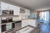 This single-floor residence offers a well-designed layout that balances functionality and contemporary style. The kitchen is outfitted with a full suite of stainless steel appliances, including a refrigerator, range, microwave, and dishwasher, complemented by white cabinetry, granite-style countertops, a subway tile backsplash, and warm wood-style flooring. A built-in wine rack adds a distinctive touch to the upper cabinetry.

The living area is bright and inviting, featuring large sliding glass doors that open to a private balcony with open outdoor views. Sheer curtains frame the doors, allowing ample natural light to fill the space.

The bedroom is finished with plush carpeting, a ceiling fan, and a window offering additional natural light and outdoor views. It connects directly to a walk-through closet and an en-suite bathroom. The bathroom features a white vanity with granite-style countertops, wood-style flooring, and a shower-tub combination enclosed by a curtain. Neutral taupe and gray tones are carried consistently throughout the unit, creating a cohesive and calm aesthetic overall.