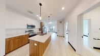This single-floor unit showcases a thoughtfully designed open-concept layout with a contemporary aesthetic. The kitchen serves as the centerpiece, featuring a substantial island topped with elegant veined quartz countertops and an undermount sink paired with a matte black gooseneck faucet. Cabinetry combines crisp white upper cabinets with warm wood-toned lower cabinets, creating a striking two-tone contrast. Stainless steel appliances, including a range, microwave, and refrigerator, complete the functional cooking space. Pendant lights with glass shades hang above the island, adding warmth to the clean-lined design.

Light hardwood flooring extends throughout, enhancing the sense of openness as the kitchen flows seamlessly into the living area. Large windows allow generous natural light to fill the space, offering views of the surrounding area. Recessed lighting supplements the natural light throughout.

The bathroom maintains the same modern design language, featuring a wood-toned floating vanity topped with quartz, a matte black faucet, a large mirror, and a glass-enclosed walk-in shower with white tile. White walls and light flooring keep the space feeling clean and bright. Overall, the unit delivers a cohesive, modern living environment with quality finishes throughout.