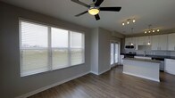 This single-floor residence offers a thoughtfully designed open-concept layout that seamlessly connects the living and kitchen areas. The living space features warm hardwood-style flooring, neutral gray walls, and crisp white baseboards that create a clean, contemporary aesthetic. A ceiling fan with an integrated light fixture anchors the living area, providing both comfort and style. Large horizontal blinds dress the expansive windows, allowing generous natural light to fill the interior while offering privacy and light control.

The kitchen is positioned adjacent to the living area and is outfitted with white cabinetry, stainless steel appliances including a microwave and range, and a kitchen island with pendant lighting above. Track lighting further illuminates the kitchen workspace, adding a modern touch. A second windowed door provides additional access and light to the space.

The overall ambiance is bright, airy, and move-in ready, with a cohesive neutral color palette that lends itself well to a variety of furnishing styles. The open flow between living and kitchen areas makes the space feel expansive and functional, ideal for both everyday living and entertaining.