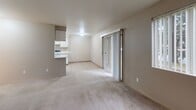 This single-floor residence offers a practical and comfortable layout designed for everyday living. The open living area is generously sized, featuring neutral-toned carpet, a wall-mounted fireplace, and a sliding glass door that fills the space with natural light and provides access to the outdoors. The galley-style kitchen is efficiently organized, with ample white cabinetry lining both walls, light countertops, a double stainless steel sink, a dishwasher, and a full suite of white appliances including a range and refrigerator. Tile flooring runs throughout the kitchen for easy maintenance. The space includes two carpeted bedrooms, each finished with neutral walls and windows that invite natural light. One bedroom features a sliding-door closet, while another offers open access to adjoining spaces. Two bathrooms serve the home: one full bathroom with a soaking tub, a single vanity, and tile flooring, and a second bathroom featuring a walk-in glass shower, an extended vanity with generous counter space, a large mirror, and warm lighting. Throughout the home, textured ceilings and a consistent neutral color palette create a cohesive, understated aesthetic suited to a variety of furnishing styles.