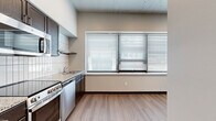 Located at 333 E East English Street in Wichita, Kansas, this one-bedroom, one-bathroom unit offers a thoughtfully designed layout that maximizes every square foot of its compact footprint. The open kitchen serves as the heart of the space, showcasing dark espresso cabinetry, stainless steel appliances including a range, dishwasher, refrigerator, and microwave, and a white subway tile backsplash that adds a clean, contemporary touch. A granite-style countertop and undermount sink complete the functional cooking area, while a large, multi-pane window fitted with horizontal blinds floods the space with natural light and provides views to the outside. Warm wood-look flooring runs seamlessly throughout the unit, creating a cohesive and inviting aesthetic. A narrow hallway connects the main living areas to the private bedroom and bathroom, with the corridor featuring a textured ceiling and built-in panel storage. The bedroom is a cozy, well-defined retreat with neutral walls and the same consistent wood-look flooring. The bathroom is clean and efficient, featuring a walk-in shower with white acrylic surround, chrome fixtures, and a toilet, all finished with matching wood-look flooring and dark baseboards. The exposed concrete ceiling elements throughout lend an industrial character to the overall design.