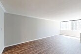 Located at 1270 W Peachtree St NW in the heart of Atlanta, GA, this one-bedroom, one-bathroom residence offers a well-organized single-floor layout with a clean, modern aesthetic. The spacious living room is a standout feature, showcasing rich, dark hardwood-style flooring, soft neutral gray walls, and crown molding details. A large corner window floods the room with natural light while framing city views, creating an open and airy atmosphere. The living area flows seamlessly toward the kitchen, which is equipped with a refrigerator, range, and cabinetry, making efficient use of the available space. A hallway connects the main living area to the private bedroom, which is finished with plush wall-to-wall carpeting and features a generous double-door closet for ample storage. A large window in the bedroom continues the theme of natural light and city views. The bathroom is well-appointed with large-format neutral tile surrounding a full soaking tub and shower combination, complemented by wood-look flooring and a dark-toned vanity with a stone countertop. Throughout the residence, white trim and neutral tones create a cohesive, move-in-ready environment ideal for urban living in Midtown Atlanta.