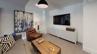 This thoughtfully designed single-floor space seamlessly blends open-plan living with flexible, defined zones. The main area combines a lounge and dining space, unified by neutral carpet flooring, recessed lighting, and a muted gray-and-white color palette that creates a clean, contemporary backdrop. Large floor-to-ceiling windows dressed with teal drape panels allow generous natural light to fill the interior while framing outdoor views, contributing to an airy, welcoming atmosphere.

A standout architectural feature is the set of sliding glass barn doors with dark wood frames and black industrial hardware, which connect the main living area to an adjacent space. These doors offer the ability to open the layout for a more expansive feel or close it off for privacy, adding both function and visual character to the design.

The lounge area is anchored by a neutral sofa accessorized with bold throw pillows, alongside a rustic wood console table adorned with potted greenery and curated artwork. A dedicated media nook features a wall-mounted flat-screen television, a low white credenza, a leather lounge chair, and a warm wood coffee table, creating an intimate retreat within the broader space. Together, these zones offer a cohesive and versatile environment suited for both relaxation and gathering.