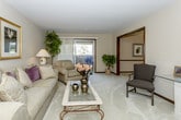This single-floor residence offers a thoughtfully designed layout with a comfortable blend of functional and formal living spaces. The living room features plush carpeting, a built-in bookshelf, and a sliding glass door that brings in natural light and provides access to an outdoor area. Framed artwork and warm neutral tones contribute to a welcoming ambiance throughout.

The formal dining room is highlighted by an elegant chandelier and a glass-top dining table, with dark wood trim framing the doorways and adding a polished touch. Adjacent to the kitchen, a casual breakfast area with tile flooring accommodates a round glass table and rattan chairs beneath a ceiling fan. The kitchen features dark wood cabinetry, tile flooring, and a window above the sink.

The primary bedroom offers carpeted flooring, a large window with wood-trimmed blinds, and ample space for a full dresser with mirror. A second bedroom provides a cozy retreat with warm lamp lighting and coordinating wood furnishings. Both bathrooms include light-colored vanities with generous countertop space and large mirrors. Overall, the residence presents a cohesive, traditionally styled interior with consistent finishes throughout.