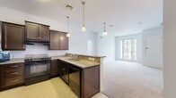 This single-floor residence offers a thoughtfully designed open-concept layout that seamlessly connects the kitchen and living area. The kitchen is a standout feature, appointed with rich dark espresso cabinetry, granite countertops, a peninsula with bar seating, and black appliances including a gas range, refrigerator, microwave, and dishwasher. Pendant lighting above the peninsula adds warmth, while tile flooring grounds the space. The adjoining living area flows naturally from the kitchen and is finished with plush neutral carpeting, leading to a set of French doors that invite natural light and provide outdoor access.

The bedrooms are carpeted and bright, each offering a calm, neutral palette and adequate natural light through slatted blinds. The primary bathroom is generously sized, featuring an extended dark wood double vanity with a crisp white countertop, large mirror, and tile flooring. A secondary full bathroom mirrors the design aesthetic with a single vanity, white countertop, and clean finishes throughout.

A dedicated laundry room houses a full-size front-loading washer and dryer alongside a water heater, providing practical convenience. The consistent use of dark cabinetry, neutral tones, and tile and carpet flooring throughout gives the space a cohesive and polished character.