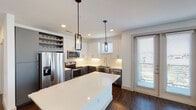 This single-floor residence showcases a thoughtfully designed layout with contemporary finishes throughout. The kitchen serves as a central highlight, featuring two-tone cabinetry with crisp white upper cabinets and charcoal lower cabinets, a white quartz island, subway tile backsplash, stainless steel appliances, and a built-in wine rack above the refrigerator. Industrial-style pendant lights add character, while dark hardwood flooring and a large window enhance the space. A dining and living area adjoins the kitchen, benefiting from sliding glass doors and additional windows that invite ample natural light and outdoor views.

The bedrooms are carpeted for comfort, each equipped with a ceiling fan and windows fitted with blinds, providing a quiet, well-lit retreat. The primary bathroom is finished with large-format light tile flooring, a dark-toned floating vanity, white countertop, tiled shower-tub combination, and direct access to a spacious walk-in closet outfitted with built-in shelving. The overall aesthetic is clean and modern, with neutral tones and quality materials creating a cohesive, move-in-ready environment throughout the unit.