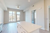 This well-designed single-floor unit offers a clean, modern aesthetic throughout, highlighted by light hardwood-style flooring, neutral wall tones, and abundant natural light. The open-concept layout connects the kitchen and living area seamlessly, creating an efficient and inviting atmosphere.

The kitchen is a standout feature, equipped with full-height white shaker cabinetry — including glass-front upper cabinets — a tiled backsplash, quartz countertops, a central island, and a complete suite of stainless steel appliances including a gas range, microwave, dishwasher, and refrigerator. Recessed lighting adds a polished finish to the space.

The living area benefits from large floor-to-ceiling windows and sliding glass doors that open to a balcony, flooding the space with natural light and offering views of the surrounding urban landscape. A ceiling fan enhances comfort in this open zone.

The generously sized primary bedroom features tall windows with city views, a ceiling fan, and light-toned flooring that carries throughout the unit. A dedicated closet provides practical storage. The overall design is clean and contemporary, making efficient use of every square foot in a bright, move-in-ready layout.