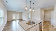 Located at 120 Lullwater Dr in Evans, Georgia, this single-floor home offers a well-designed open-concept layout that seamlessly connects the kitchen, dining, and living areas. The kitchen is a standout feature, showcasing white shaker cabinetry extending to the ceiling, granite countertops, and a large central island with a single-basin sink. Stainless steel appliances — including a French door refrigerator, range, and microwave — complement the clean, modern aesthetic. Three pendant lights with glass shades hang above the island, adding warmth and style. Durable wood-look flooring runs throughout the main living spaces, while the living area benefits from abundant natural light through multiple windows and a set of French doors, complemented by a ceiling fan overhead. A dedicated laundry closet houses a stacked washer and dryer unit for added convenience. The bedroom features plush carpeting and a bright window with outdoor views. The bathroom is finished with a tiled tub-shower combination, wood-look flooring, and granite-topped vanity. Neutral tones throughout create a bright, airy ambiance that makes the space feel welcoming and move-in ready.