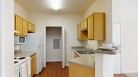 This single-floor unit offers a practical and well-organized layout designed for comfortable everyday living. The galley-style kitchen is a functional highlight, featuring warm honey-toned wood cabinetry — both upper and lower — paired with granite-look countertops and a double basin sink. White appliances, including a refrigerator, electric range, and built-in microwave, are neatly integrated throughout. Hardwood-style flooring runs the length of the kitchen, adding warmth and easy maintenance. A utility closet housing the electrical panel is conveniently accessible directly from the kitchen.

The living area is open and airy, anchored by a distinctive curved bay window arrangement that allows generous natural light to fill the room. A ceiling fan overhead adds both function and a finishing touch to the space. Plush neutral carpet extends throughout the living and bedroom areas, contributing to a cozy atmosphere.

The bedrooms are quiet and well-lit, each featuring carpeted floors and windows with blinds for privacy and light control. The bathroom is equipped with a wood-toned vanity, granite-look countertop, a large mirror with overhead lighting, hardwood-style flooring, and a shower-tub combination, offering a clean and efficient design.