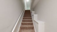 This 1,130 sq ft, 2-bedroom, 1-bathroom multi-floor residence in Glen Allen, VA offers a well-designed layout across three floors. The main level (720 sq ft) features a combined kitchen and living area anchored by a tiled fireplace with a classic mantle and durable light hardwood flooring. Crown molding and a ceiling fan add refined detail to the living space, which is brightened by multiple windows and a glass-panel door offering outdoor views. The kitchen is appointed with white shaker cabinetry, granite countertops, a peninsula with pendant lighting, and stainless steel appliances including a French door refrigerator, electric range, and built-in microwave. The upper level (340 sq ft) houses two carpeted bedrooms, each featuring vaulted ceilings, ceiling fans, and natural light from windows with outdoor views. The primary bedroom measures 180 sq ft and includes a closet. The full bathroom offers a tub/shower combination with white tile surround, hardwood flooring, and a granite-topped vanity. A utility room and additional closet provide practical storage, and a staircase connects all three levels of this thoughtfully arranged home.