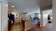 This single-floor residence at 1839 Ashton Ln in Kent, Ohio offers a well-organized, open-concept layout that connects the kitchen, dining area, and living room into one cohesive living space. The kitchen is equipped with dark granite countertops, a central island with a sink, warm wood cabinetry, black appliances including a refrigerator and microwave, and recessed lighting overhead. A dedicated dining area sits adjacent to the kitchen, providing a practical space for meals. The living room features hardwood-style flooring, a large window that allows natural light to fill the space, and a textured ceiling throughout. A stacked washer and dryer unit is conveniently integrated within the main living area. Two bedrooms offer carpet flooring, natural light through blinded windows, built-in shelving, and a built-in desk workspace in one room. Two full bathrooms feature granite-topped vanities with wood cabinetry, tile flooring, large mirrors with overhead lighting, and ample storage. The overall ambiance is functional and comfortable, well-suited for everyday living in the Kent, Ohio area.
