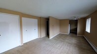 This single-floor residence offers a straightforward and functional layout designed for comfortable everyday living. The interior is finished in warm, neutral beige tones throughout, creating a cohesive and understated ambiance across all areas of the home. The main living area features soft wall-to-wall carpeting that transitions seamlessly into tile flooring in adjoining spaces, providing both comfort and practicality depending on the area's use. A prominent double-door closet with white panel doors offers generous built-in storage, making efficient use of the available wall space. The textured white ceilings add a classic residential character to the interior. A ceiling fan is visible in the adjoining area, providing air circulation throughout the connected spaces. Doorways lead to additional rooms and corridors, suggesting a well-connected floor plan that flows naturally from one area to the next. White baseboards trim the perimeter of each room, providing clean visual contrast against the warm-toned walls. Overall, the space presents a clean, move-in ready environment with a simple and functional aesthetic suited to a wide range of living arrangements.