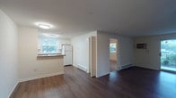 This single-floor, 1-bedroom, 1-bathroom unit offers a clean and functional layout designed for comfortable everyday living. The open living area is finished with rich, dark hardwood-style flooring that extends throughout the main spaces, creating a warm and cohesive atmosphere. A sliding glass door floods the living room with natural light and provides direct access to a private balcony with outdoor views of surrounding greenery.

The kitchen is well-equipped with white cabinetry, dark laminate countertops, a white appliance suite including a coil-burner range, over-the-range microwave, and refrigerator, complemented by a classic white tile backsplash. A pass-through counter connects the kitchen to the main living area, enhancing the open feel. A closet near the entryway provides additional storage.

The bedroom features plush wall-to-wall carpeting, a ceiling fan with integrated lighting, a window with natural light and outdoor views, and a generously sized reach-in closet with bifold doors and a built-in rod for ample storage. Baseboard heating units are present throughout the unit for efficient climate control.

The bathroom includes a full tub-and-shower combination with white tile surround, a toilet, vanity with sink, and a mirrored medicine cabinet with built-in lighting.