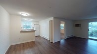 This single-floor, 1-bedroom, 1-bathroom unit offers a clean and functional layout designed for comfortable everyday living. The open living area is finished with rich, dark hardwood-style flooring that extends throughout the main spaces, creating a warm and cohesive atmosphere. A sliding glass door floods the living room with natural light and provides direct access to a private balcony with outdoor views of surrounding greenery.

The kitchen is well-equipped with white cabinetry, dark laminate countertops, a white appliance suite including a coil-burner range, over-the-range microwave, and refrigerator, complemented by a classic white tile backsplash. A pass-through counter connects the kitchen to the main living area, enhancing the open feel. A closet near the entryway provides additional storage.

The bedroom features plush wall-to-wall carpeting, a ceiling fan with integrated lighting, a window with natural light and outdoor views, and a generously sized reach-in closet with bifold doors and a built-in rod for ample storage. Baseboard heating units are present throughout the unit for efficient climate control.

The bathroom includes a full tub-and-shower combination with white tile surround, a toilet, vanity with sink, and a mirrored medicine cabinet with built-in lighting.