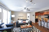 This single-floor residence offers a thoughtfully laid-out floor plan that flows naturally from room to room. The living area serves as the heart of the home, featuring rich hardwood-style flooring, a textured ceiling, and dual ceiling fans alongside track lighting. Large windows dressed with teal curtains allow generous natural light to fill the space, complementing the open dining area nearby. The kitchen is equipped with dark cabinetry, granite-style countertops, and black appliances including an electric range and full-size refrigerator. A convenient in-unit laundry area is directly accessible from the kitchen. The residence includes multiple bedrooms, each finished with plush carpeting and neutral walls that create a calm, restful atmosphere. One bedroom features rustic wood floating shelves, adding a warm, modern touch. The bathrooms are well-appointed with warm wood-toned vanities, dual sinks, granite-style countertops, large framed mirrors, and hardwood-style flooring, offering a clean and functional design. A shared bathroom hallway connects the bedroom spaces seamlessly. Throughout the home, the consistent use of warm tones, practical finishes, and ample storage creates a comfortable and cohesive living environment.