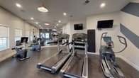 Located at 6959 Castle Ct in Frederick, MD, this single-floor fitness center offers a comprehensive workout facility designed for both cardio and strength training. The space is thoughtfully laid out, with a dedicated cardio zone featuring multiple Life Fitness treadmills, an elliptical, and a recumbent exercise bike, ensuring a full range of aerobic options for users of all fitness levels. Wall-mounted flat-screen TVs are positioned throughout, allowing members to stay entertained during their workouts.

The strength training area is equipped with a multi-station cable machine, a leg press, a rowing machine, and a dumbbell rack, providing ample options for resistance training. A large floor-to-ceiling mirror spans one wall, visually expanding the space and allowing users to monitor their form. The durable rubber flooring throughout is practical and well-suited for a high-activity environment.

Design details elevate the space beyond a typical gym. A bold chevron accent wall in dark teal and white anchors the strength zone, adding a dynamic visual element. Warm pendant lighting complements recessed ceiling lights, creating a balanced and inviting ambiance. Natural light filters in through multiple windows, and a dedicated exit door provides convenient access. Posted fitness center rules ensure a well-managed, community-friendly environment.