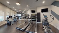 Located at 6959 Castle Ct in Frederick, MD, this single-floor fitness center offers a comprehensive workout facility designed for both cardio and strength training. The space is thoughtfully laid out, with a dedicated cardio zone featuring multiple Life Fitness treadmills, an elliptical, and a recumbent exercise bike, ensuring a full range of aerobic options for users of all fitness levels. Wall-mounted flat-screen TVs are positioned throughout, allowing members to stay entertained during their workouts.

The strength training area is equipped with a multi-station cable machine, a leg press, a rowing machine, and a dumbbell rack, providing ample options for resistance training. A large floor-to-ceiling mirror spans one wall, visually expanding the space and allowing users to monitor their form. The durable rubber flooring throughout is practical and well-suited for a high-activity environment.

Design details elevate the space beyond a typical gym. A bold chevron accent wall in dark teal and white anchors the strength zone, adding a dynamic visual element. Warm pendant lighting complements recessed ceiling lights, creating a balanced and inviting ambiance. Natural light filters in through multiple windows, and a dedicated exit door provides convenient access. Posted fitness center rules ensure a well-managed, community-friendly environment.