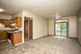 This single-floor residential unit offers a practical and comfortable layout designed for everyday living. The open-concept living and dining area is anchored by plush carpeting and transitions seamlessly into a tiled entryway and kitchen zone. A ceiling fan overhead and a sliding glass door leading to a private balcony fill the living space with natural light and provide pleasant outdoor views of the surrounding greenery. The kitchen is well-appointed with warm oak cabinetry, dark laminate countertops, a double stainless steel sink with under-cabinet lighting, and a freestanding electric range, offering ample storage and prep space. A secondary living or flex area connects to the kitchen, providing additional versatile space. The two bedrooms are carpeted and feature neutral walls with wood-trimmed windows that let in natural light; one bedroom includes a walk-in closet with built-in shelving for added storage convenience, while the other features a built-in window bench. The full bathroom is finished with tile flooring, a wood-trimmed vanity with a light stone-tone countertop, a large mirror, and a glass-door shower and tub combination. Throughout the unit, warm wood door and window trim provides a cohesive, classic aesthetic.