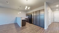 This single-floor residence offers a thoughtfully designed open-concept layout that seamlessly connects the kitchen and living areas. The kitchen is a standout feature, showcasing rich dark cabinetry that extends floor-to-ceiling for generous storage, a contrasting kitchen island with a light stone countertop, black appliances, and stylish pendant lighting complemented by an elegant chandelier overhead. Durable wood-look flooring runs throughout the main living spaces, adding warmth and visual continuity.

The living area is spacious and open, with neutral-toned walls and clean lines that create a bright, welcoming atmosphere. A hallway connects the main living space to the private quarters, where multiple bedrooms are finished with plush carpeting, ceiling fans, and windows fitted with blinds that allow for natural light. Each bedroom offers closet space, with at least one room featuring a dedicated walk-in style closet with built-in rod storage.

The residence includes two full bathrooms, each equipped with a soaking tub and shower combination, chrome fixtures, and wood-look flooring that ties back to the rest of the home's design palette. The overall aesthetic is modern and functional, with a clean, neutral color scheme that provides a versatile backdrop throughout.