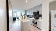 This thoughtfully designed one-bedroom, two-bathroom high-rise unit offers an efficient yet refined layout across a single floor. Light white oak hardwood flooring runs throughout, unifying each space and complementing the clean, contemporary aesthetic.

The open-concept kitchen and living area serves as the heart of the unit. The kitchen is outfitted with tall grey shaker-style cabinetry extending to the ceiling, a dark glossy subway tile backsplash, stainless steel gas range, integrated refrigerator, and a white quartz waterfall island with bar seating. A stacked in-unit washer and dryer is conveniently tucked behind a louvered closet door nearby.

The living area benefits from expansive floor-to-ceiling windows that frame sweeping urban skyline views, flooding the space with natural light throughout the day.

The bedroom features the same generous window configuration, offering additional city views and abundant daylight. A dedicated closet provides practical storage.

Both bathrooms are finished with large-format dark marble-style wall tiles, white vanities, and soaking tub and shower combinations, delivering a polished, spa-like atmosphere. The overall design is bright, modern, and efficiently organized.