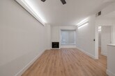 Located in the heart of Los Angeles at 1440 N Alta Vista Blvd, this single-floor residence showcases a clean, modern aesthetic defined by crisp white walls, light wood flooring, and recessed accent lighting throughout. The open living area serves as the centerpiece of the home, anchored by a sleek built-in fireplace and a large window fitted with a roller shade that softens incoming natural light. The galley-style kitchen is thoughtfully appointed with white flat-front cabinetry, white quartz countertops, under-cabinet lighting, and a full suite of stainless steel appliances including a gas range, over-the-range microwave, and French door refrigerator. A peninsula counter provides additional workspace and a natural transition into the living space. The bedrooms continue the home's minimalist design, each featuring light wood flooring, recessed linear lighting, and generous closet space — including a mirrored sliding-door closet and a walk-in with built-in shelving. A ceiling fan adds comfort to one bedroom. The bathroom is elegantly finished with marble-patterned tile flooring and surround, a glass-enclosed tub and shower, a floating white vanity, and an illuminated mirror, completing the home's cohesive, contemporary character.