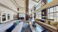 Located at 7500 Hearthside Way in Elkridge, Maryland, this elegantly designed two-floor community space offers an impressive blend of upscale architectural details and functional amenities across a generous footprint spanning both levels.

The centerpiece of the main floor is a grand living area distinguished by soaring double-height ceilings, rich dark hardwood flooring, and dramatic floor-to-ceiling windows that flood the interior with abundant natural light. A striking stacked-stone fireplace serves as a focal point, framed by a wood mantel and large-scale artwork above, with refined seating arrangements anchored by patterned area rugs. Elegant chandeliers and wall sconces provide warm accent lighting throughout.

The open-plan layout flows seamlessly into a dining area furnished with a substantial wood table and sleek modern chairs, alongside a casual high-top bar seating area positioned against the expansive window wall. A billiards table adds a recreational dimension to the space.

The kitchen is well-appointed with warm cherry wood cabinetry, granite countertops, stainless steel appliances including a refrigerator and dishwasher, and dark hardwood flooring, offering a fully functional service area.

Dark wood-paneled columns punctuate the space, reinforcing the sophisticated aesthetic, while the upper floor provides additional square footage overlooking the dramatic main level below.
