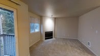 This single-floor space presents a well-maintained living area designed with a neutral and functional aesthetic. The main living room is finished with wall-to-wall carpet in a warm beige tone, contributing to a comfortable and quiet atmosphere underfoot. Walls are painted in a soft, light neutral hue that enhances the sense of openness and pairs seamlessly with the overall color palette.

A built-in fireplace serves as a focal point of the living room, framed by a clean, understated surround that adds a touch of architectural character without overwhelming the space. The fireplace provides both a practical heating source and a natural gathering point within the room.

Natural light enters through a window fitted with horizontal blinds, allowing for adjustable privacy and light control. The window offers a view of surrounding greenery, bringing a subtle connection to the outdoors. Overhead, a flush-mounted ceiling light provides consistent ambient illumination throughout the space.

The overall design is straightforward and versatile, with minimal ornamentation that allows for flexible furnishing arrangements. The space presents a clean, move-in-ready condition well-suited to a variety of interior styles.