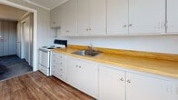 Located at 1 Carleton Rd in Storrs Mansfield, Connecticut, this single-floor home offers a straightforward and functional layout throughout. The interior is defined by a consistent design language of vertical board-and-batten wall paneling in a neutral gray tone, creating a cohesive look from room to room.

The kitchen is well-equipped with white cabinetry extending from floor to ceiling, offering generous storage space. Warm butcher block countertops provide a natural contrast to the white finishes, complemented by a stainless steel sink and a white electric range. The kitchen features durable hardwood-style flooring that adds warmth to the space.

Multiple bedrooms are carpeted in a muted gray-blue tone and receive natural light through framed windows that look out to wooded surroundings. The bedrooms offer practical storage with built-in closets, including both reach-in and sliding-door closet configurations, as well as open shelving units in one of the larger rooms.

The bathroom maintains a clean, minimal aesthetic with light wood-look flooring, a white vanity, and a window that allows natural light to brighten the space.

Throughout the home, the consistent use of gray paneled walls, white trim, and natural light from multiple windows creates a calm and cohesive atmosphere suited to comfortable everyday living.