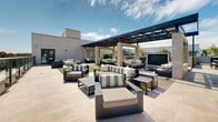 Located in the vibrant SoMa neighborhood of San Francisco, this rooftop terrace at 1140 Harrison Street offers a thoughtfully designed outdoor space with sweeping panoramic views of the city skyline, including iconic landmarks such as Salesforce Tower. The terrace is laid out across a generous open-air footprint with large-format porcelain tile flooring throughout, creating a clean and modern aesthetic.

The space is organized into several distinct zones designed for a variety of uses. A built-in bar counter with bar stools provides an ideal setting for casual gatherings, while a dedicated lounge area features built-in seating with cushions and a coffee table, anchored by a raised platform. A stretch of lush artificial turf adds a refreshing green element alongside bistro-style seating for more intimate moments.

A shaded pergola zone offers a covered retreat furnished with ample lounge seating in striped upholstery and a flatscreen display, making it well-suited for both relaxed socializing and outdoor screenings. Overhead string lighting throughout the terrace creates a warm ambiance after sunset. Mature potted trees and planters add greenery and privacy, complementing the open sky above. The glass railing system around the perimeter ensures unobstructed views of the San Francisco skyline from every vantage point.