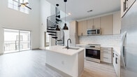 Located at 311 Karl Linn Dr in North Chesterfield, VA, this modern two-story home offers 2 bedrooms and 2 bathrooms across a thoughtfully designed layout. The main floor commands attention with soaring ceilings that amplify the sense of openness, anchored by a dramatic black spiral staircase that serves as both a functional and architectural centerpiece. Light wood-tone flooring runs throughout the main level, complementing the bright, airy atmosphere.

The contemporary kitchen is a standout feature, showcasing a large white quartz island with an undermount sink and matte black faucet, warm-toned flat-front cabinetry, a classic white subway tile backsplash, and a full suite of stainless steel appliances. Sleek black pendant lights hang above the island, adding a bold design contrast. The living area opens to a private outdoor balcony through sliding glass doors, bringing in natural light and exterior views.

Upstairs, the two bedrooms offer plush carpeting, natural light from windows with blinds, and ceiling fans. The bathrooms are finished with clean, modern details including white quartz vanity tops, warm cabinetry with matte black hardware, large framed mirrors, and wood-look flooring. Each bedroom is served by a dedicated closet, completing this well-appointed home.