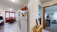 This single-floor residence offers a practical and comfortable layout across a thoughtfully arranged floor plan. The combined kitchen and dining area serves as a central hub, featuring a galley-style kitchen with rich wood cabinetry, a white appliance suite including an electric range and full-size refrigerator, and light tile flooring. The adjacent dining space is accented by deep-toned curtains and a window that brings in natural light, creating a warm and inviting atmosphere for meals.

The office area provides a dedicated workspace separate from the living quarters, enhancing the overall functionality of the home. The living room is generously proportioned, with wall-to-wall carpeting, multiple windows allowing ample natural light, and a textured ceiling that adds character to the space.

The bedroom is a comfortable retreat, featuring carpet flooring, windows dressed with lace curtains, and a baseboard heating system. The full bathroom is finished with classic white wall tile surrounding a tub-shower combination.

A hallway connects the rooms efficiently, featuring a closet for added storage. Throughout the residence, neutral wall tones and consistent finishes create a cohesive and livable environment suited for everyday comfort.